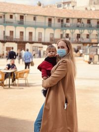 Portrait of young woman standing against building in city