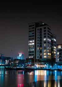 Illuminated buildings by river against sky at night