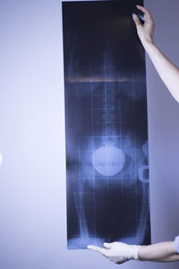 Cropped hands of woman holding x-ray image against wall