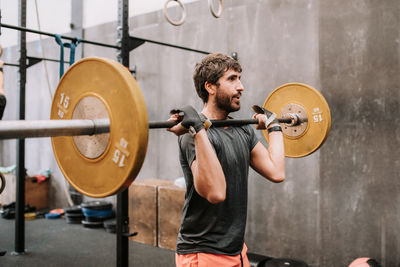 Side view of muscular male athlete doing clean and jerk exercise while training in modern fitness center