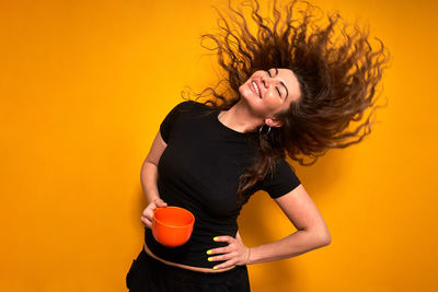 Young woman in casual clothes with an orange mug in her hand with coffee she has drunk and enjoys