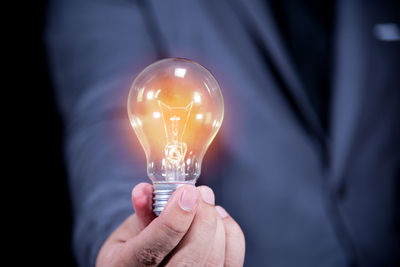 Midsection of businessman holding illuminated light bulb