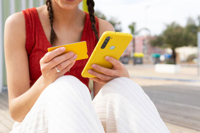 Crop view of anonymous female paying for order with plastic card during online shopping via smartphone while sitting on street