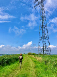 Rear view of woman in a green rural landscape walking towards a huge electricity pylon