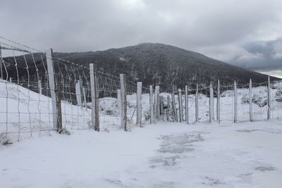 Fence on snow covered field against sky