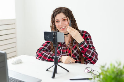 Portrait of smiling woman holding smart phone while sitting on table