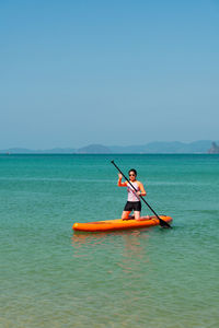 Young sporty woman playing stand-up paddle board on the blue sea in sunny day of summer vacation