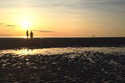 Two silhouette people walking on beach at sunset