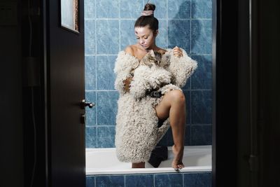 Woman wearing warm clothing while holding cat in bathtub