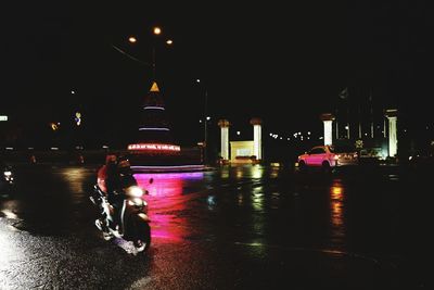Man on wet road against illuminated city at night