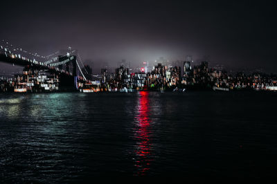 Illuminated bridge over river against buildings at night