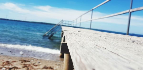 Wooden railing on beach against sky