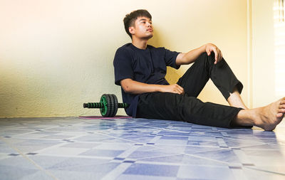 Full length of young man sitting on wall at home