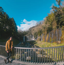 Man standing by railing against trees and mountains against sky