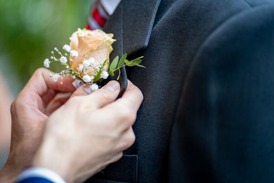 Cropped man fixing rose on friend suit