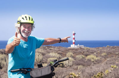 Portrait of smiling senior man with bicycle standing against sea