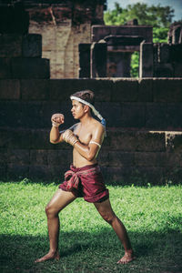 Full length of shirtless man standing against brick wall