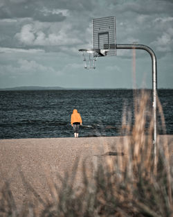 Rear view of man standing on beach against sky