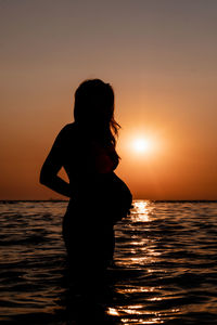 Silhouette pregnant woman standing in sea during sunset