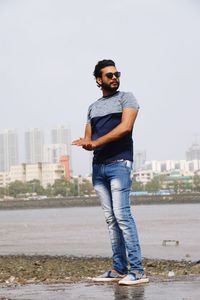 Full length portrait of young man standing against sky in city