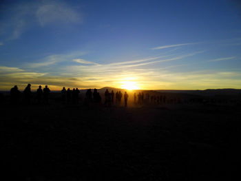 Silhouette people on landscape against sky during sunset