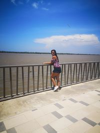 Full length of woman standing on railing against sea