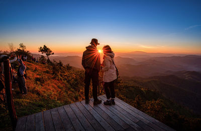 Rear view of people on mountain against sky during sunset