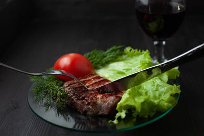 A delicious slice of steak on a plate with lettuce and tomato. knife and fork are stuck in the meat.