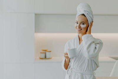 Portrait of smiling young woman with medical eye patches holding coffee cup at home