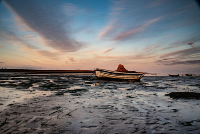 Boat on beach against sky during sunset