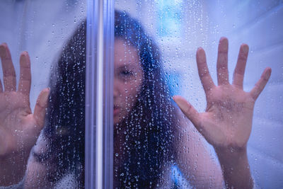 Portrait of woman seen through wet glass window