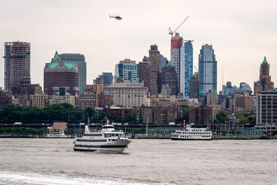 Boats in river by buildings in city against sky