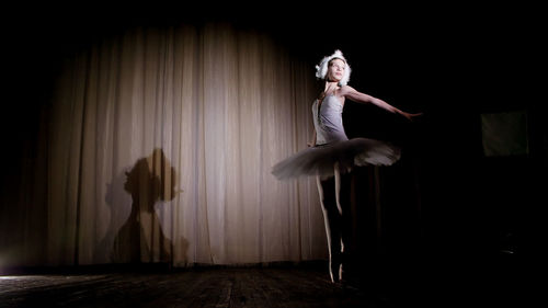  on the stage of the old theater hall. young ballerina in suit of white swan and pointe shoes