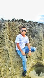 Portrait of man wearing sunglasses standing on rock against sky