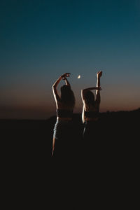 Silhouette women with arms raised against sky during dusk