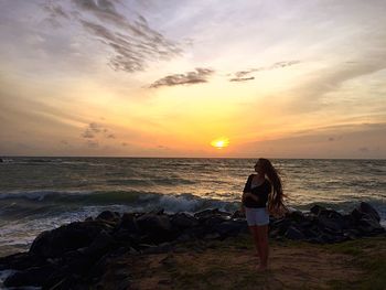 Rear view of woman standing on beach during sunset