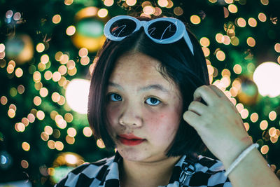 Close-up portrait of woman against illuminated lighting equipment at night