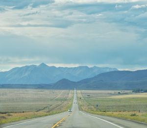 Empty road leading towards mountains against sky