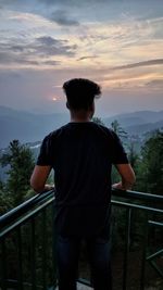 Rear view of man standing by railing against sky