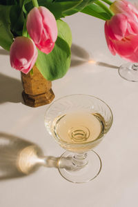 Pink tulip bouquet in vase with white wine in vintage coupe glass