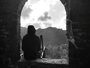 Rear view of man sitting on window sill