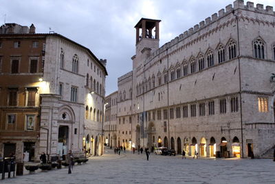 People on street amidst buildings in city at dusk