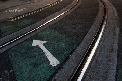 High angle view of arrow symbol on city street amid railroad tracks 