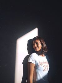 Portrait of a smiling young woman standing against wall