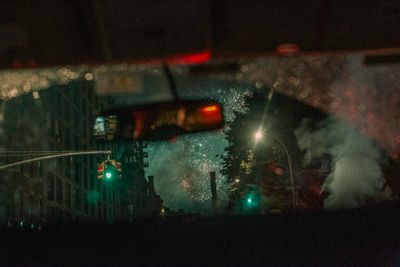 Cars on illuminated street seen through wet glass