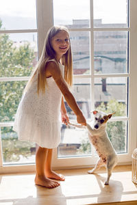 Girl in a white dress stands on the windowsill with a dog