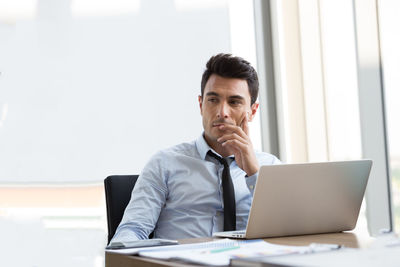 Thoughtful businessman with laptop on desk sitting in office