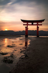 View of tori gate at beach against sky during sunset