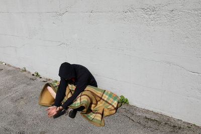 Man sitting on footpath against wall