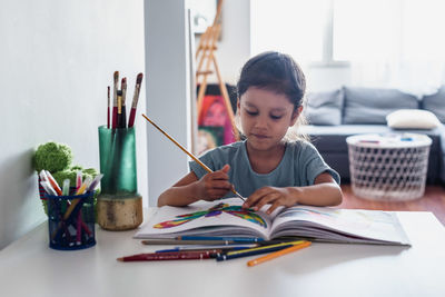 Little girl sitting at the table. she is painting pictures of animals.